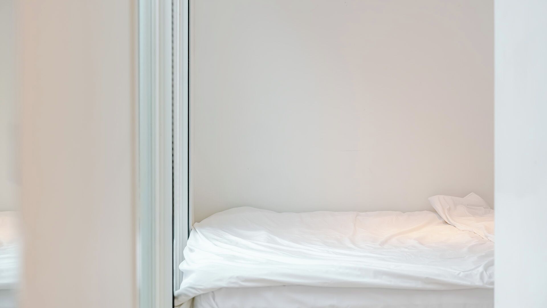 Una cama individual con ropa de cama blanca en una habitación con paredes blancas lisas.