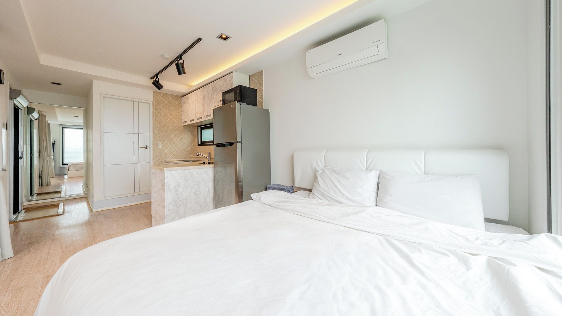 A modern hotel room with a large bed, a kitchenette, and a bathroom.