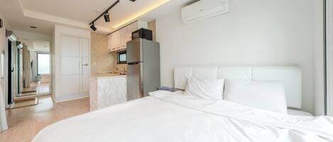 A modern hotel room with a large bed, a kitchenette, and a bathroom.