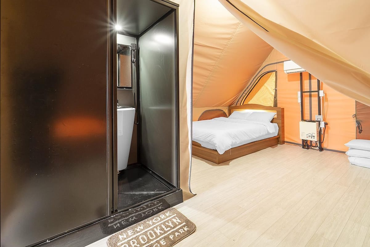 Ein Zeltraum mit Bett, kleinem Tisch und Duschbereich.