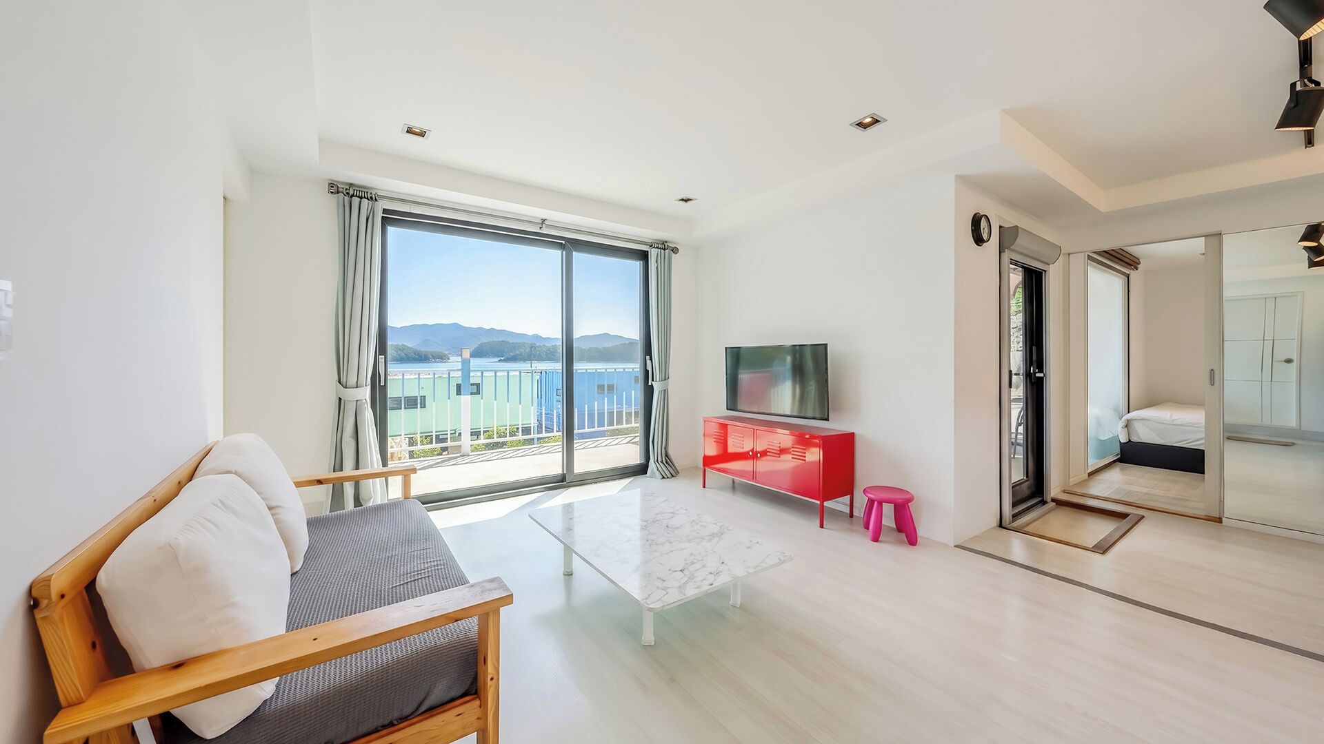 A modern living room with a large window, a flat-screen TV, a red cabinet, and a wooden chair.