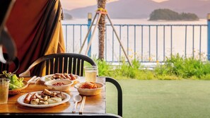 Een eettafel met eten en drinken, met uitzicht op een waterpartij en bergen.