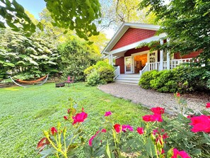 A house with a red roof, a porch, and a well-maintained garden with flowers and a hammock.