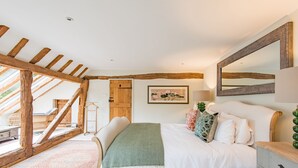 Un dormitorio con techo de madera, una cama con ropa de cama blanca, un plaid verde y un espejo grande.