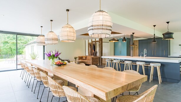 Una cocina moderna con una isla grande de madera, sillas de mimbre y luces colgantes.