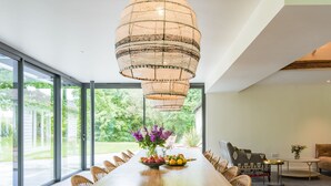 Un comedor moderno con una mesa de madera larga, sillas de mimbre y una lámpara colgante.