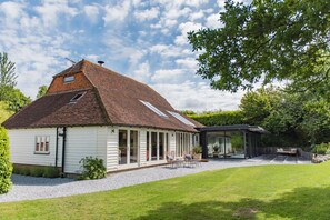 Ein Haus mit geneigtem Dach, einer überdachten Terrasse und einem gepflegten Rasen.
