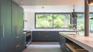 Cocina moderna con armarios oscuros, un ventanal y vistas al verdor exterior.