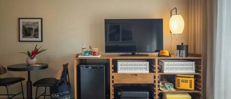 A hotel room with a television, a small table with chairs, a plant, a suitcase, and storage boxes.