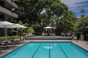 A swimming pool with lounge chairs and umbrellas, surrounded by lush greenery and trees.