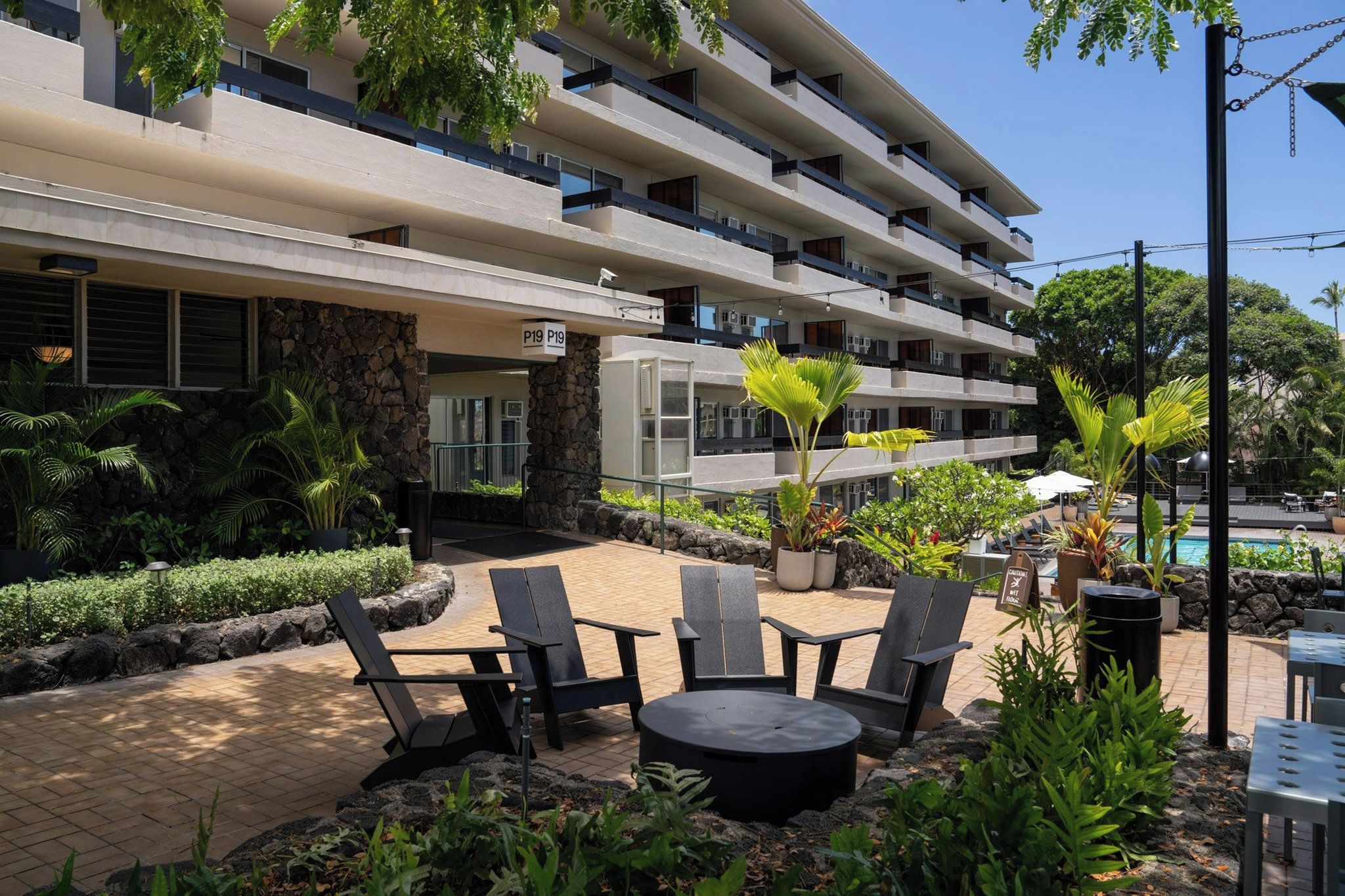 A hotel with outdoor seating, a pool, and lush greenery.