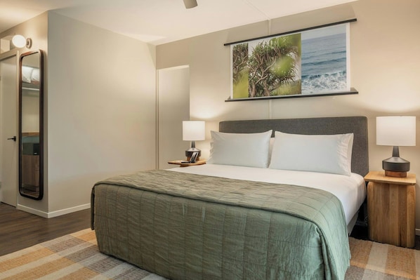 Habitación de hotel con cama, dos lámparas de noche, mesita de noche, espejo y un cuadro en la pared.