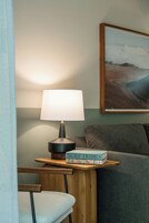 Una habitación con una lámpara sobre una mesita de madera, un libro titulado 'SURF TRIBE' en la mesa, un sofá y un cuadro en la pared.