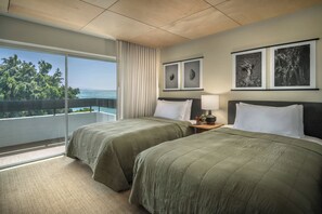 Een hotelkamer met twee bedden, een groot raam met uitzicht op bomen en de zee, en twee ingelijste foto's aan de muur.