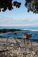 Una bicicleta con una cesta de madera estacionada en una playa rocosa con el océano al fondo.