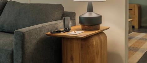 A modern living room with a grey sofa, a wooden side table with a lamp, and two framed pictures on the wall.