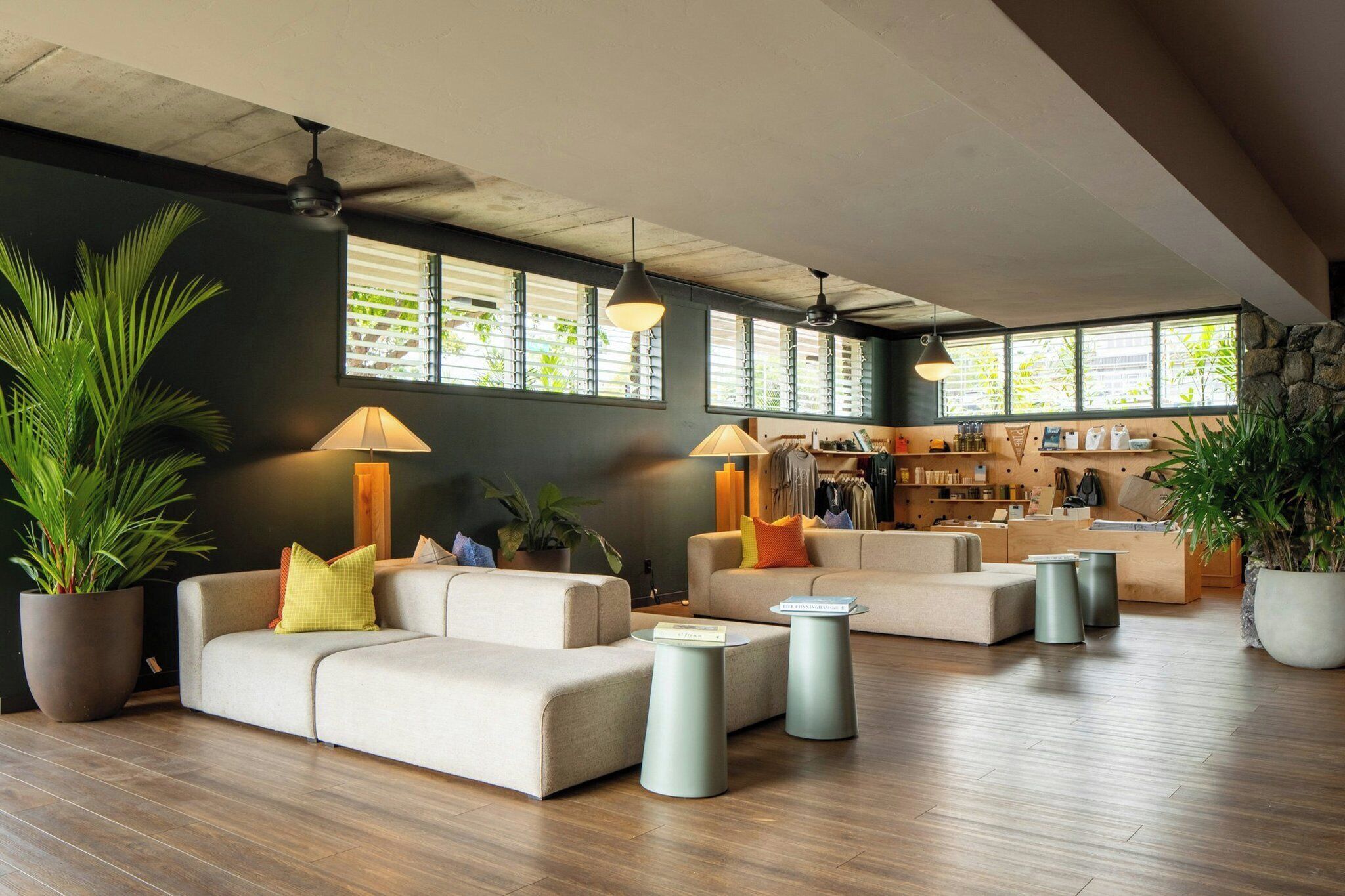 Amplia sala de estar con un conjunto de sofás, una mesa de centro y una zona de estar con una mesita. Hay plantas en macetas y un muro de piedra decorativo.