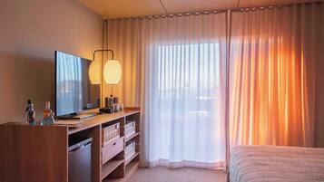 Ett hotellrum med en säng, ett skrivbord med en dator, en tv och ett fönster med gardiner.