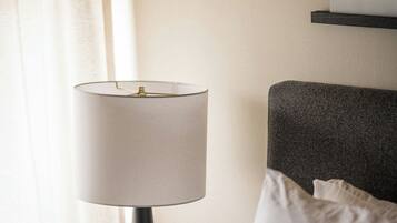 A neatly made bed with a white pillow, a bedside table with a lamp, a phone, and a power strip.