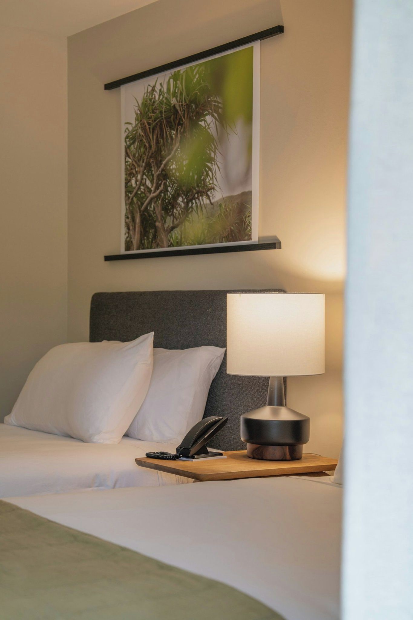 A hotel room with a bed, a bedside table with a lamp, a telephone, and a framed picture on the wall.