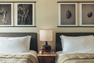 A hotel room with two beds, a nightstand with a lamp, and three framed pictures on the wall.