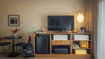 A hotel room with a television, a small table with chairs, a plant, a suitcase, and storage boxes.