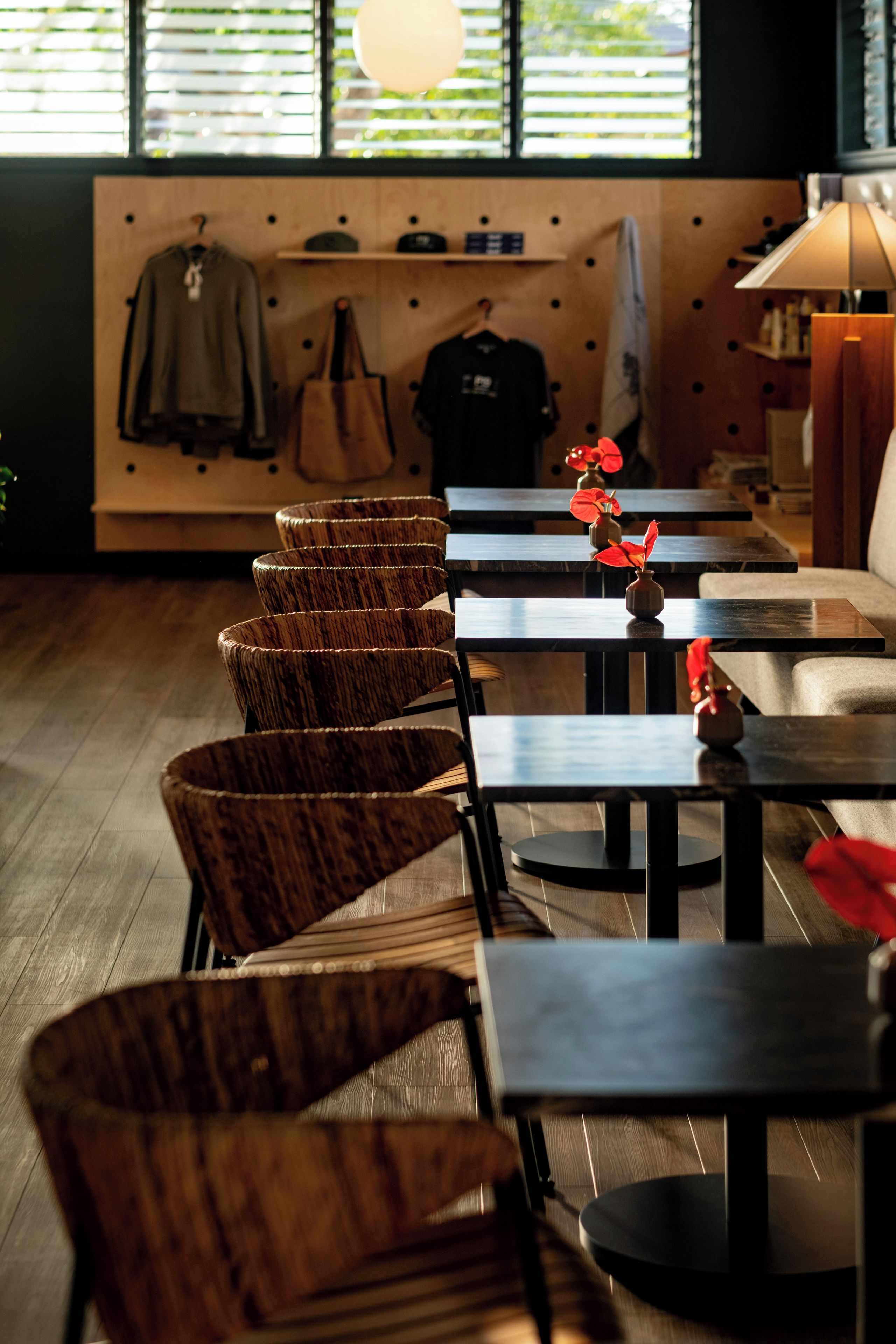 A restaurant interior with wooden chairs and tables, a wall with hanging items, and a window with blinds.