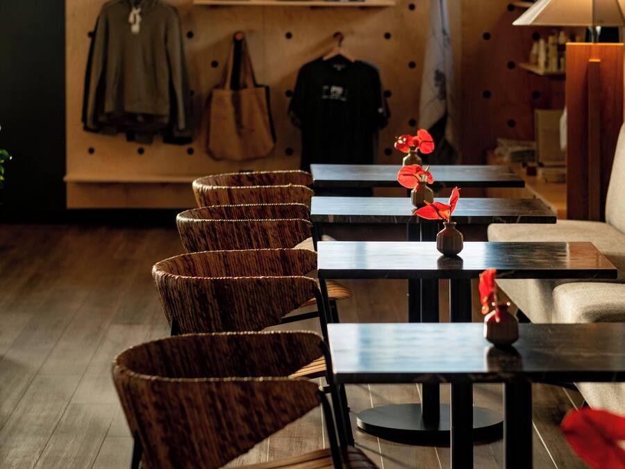 A restaurant interior with wooden chairs and tables, a wall with hanging items, and a window with blinds.