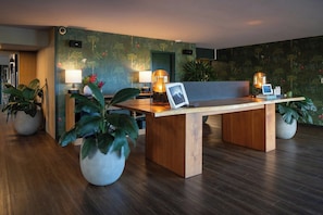 A reception desk with two lamps, a laptop, and a framed picture. There are potted plants on either side of the desk. - PACIFIC 19 Kona (Kailua-Kona)