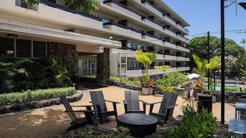 A hotel with outdoor seating, a pool, and lush greenery.