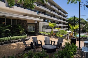 Un hotel con terraza exterior, piscina y abundante vegetación.