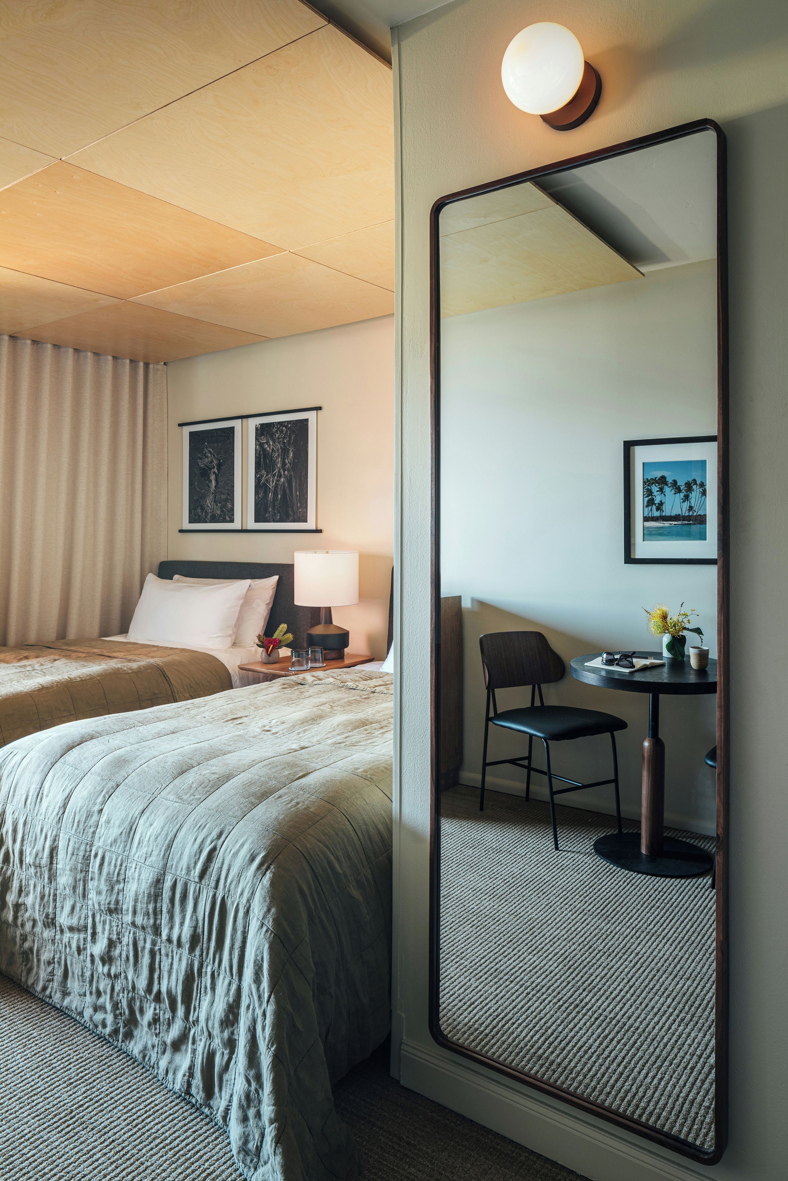 Habitación de hotel con dos camas, un escritorio con silla, un espejo grande y obras de arte en la pared.