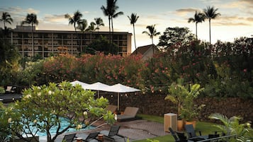 A pool area with lounge chairs, a large umbrella, and a stone wall.
