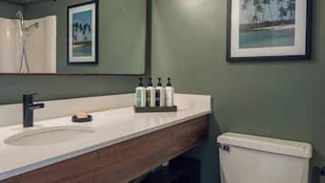 A bathroom with a wooden vanity, a white toilet, a framed picture of a beach, and a mirror with a light fixture.