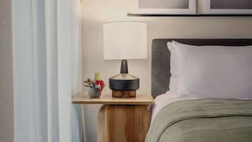A hotel room with a bed, a nightstand with a lamp, a small plant, and two wall-mounted pictures.