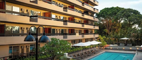 A multi-story hotel with a swimming pool, outdoor seating, and lush greenery.