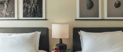 Una habitación de hotel con dos camas, una mesita de noche con lámpara y tres cuadros en la pared.