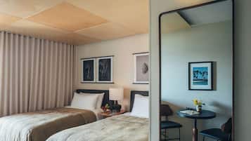 Een hotelkamer met twee bedden, een nachtkastje met een lamp, een klein rond tafeltje met een stoel, en wanddecoratie.