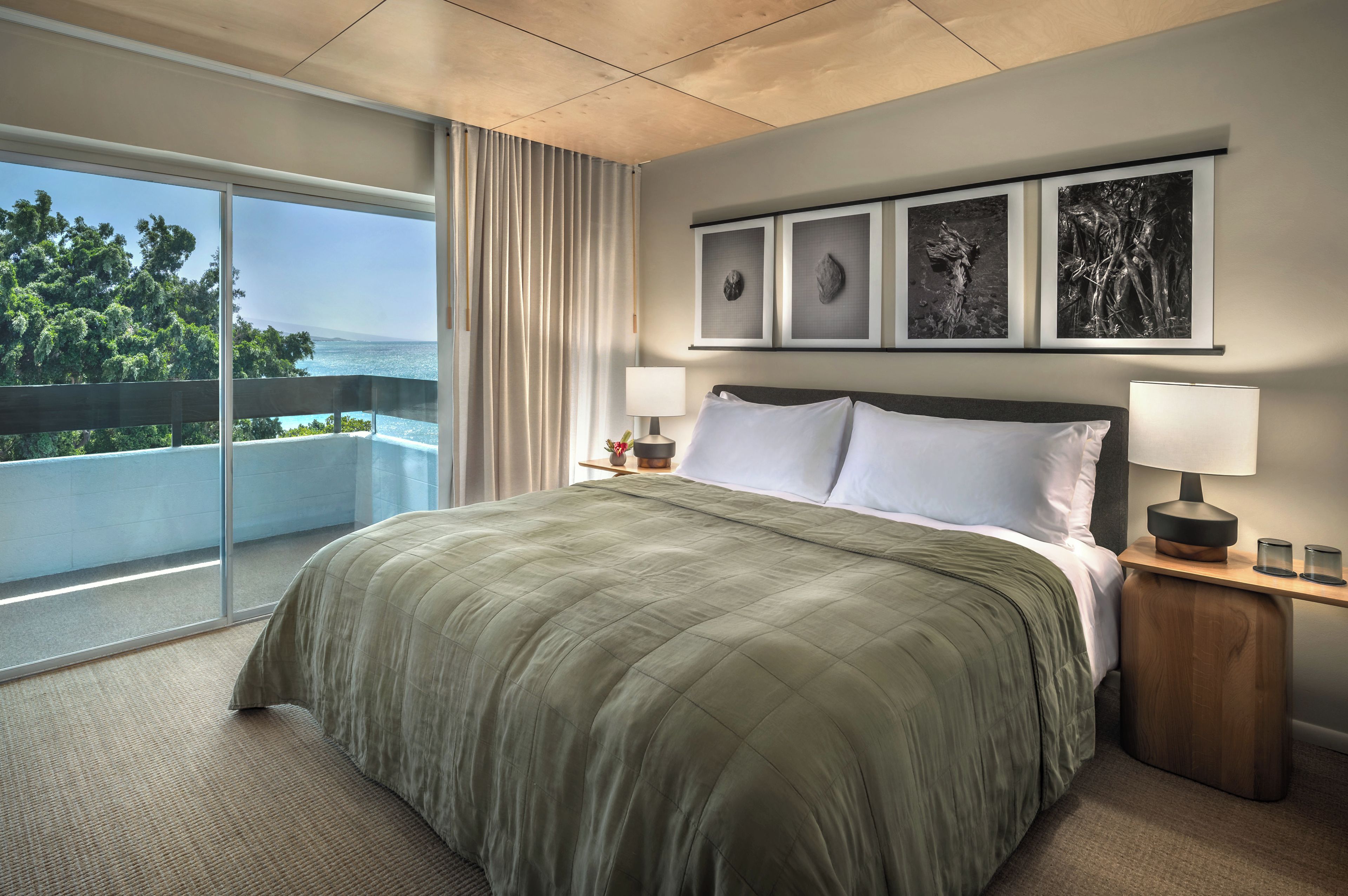 A hotel room with a large bed, a view of the sea, and three framed artworks on the wall.