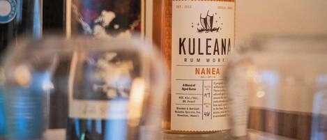 Una botella de ron Kuleana con etiqueta, una botella de otra bebida espirituosa y un vaso en primer plano.