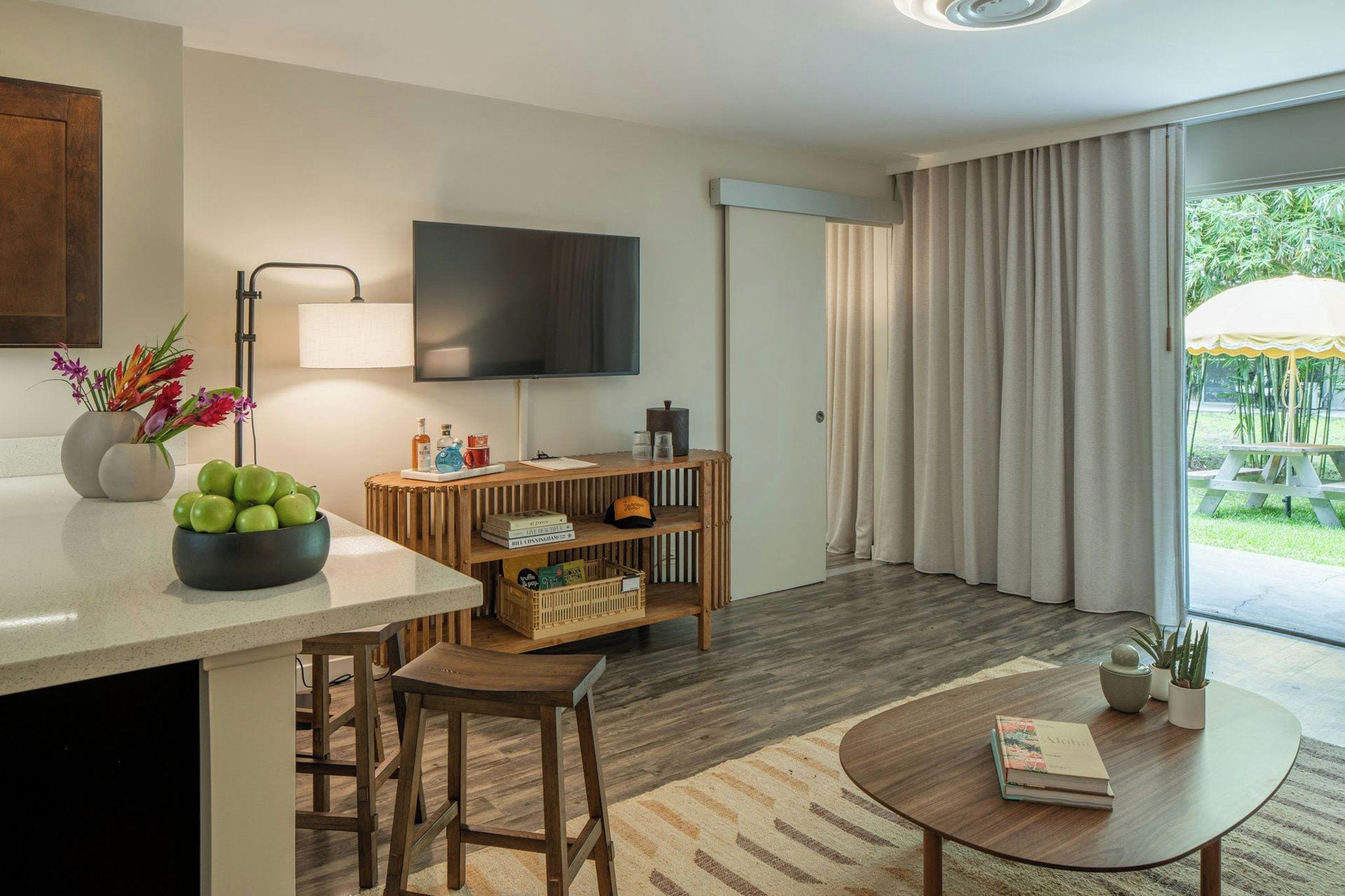 Ein modernes Wohnzimmer mit Flachbildfernseher, Couchtisch aus Holz, Bar und einer Glasschiebetür, die zu einem Außenbereich führt.