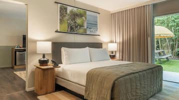 A bedroom with a bed, two bedside tables with lamps, a nightstand, a window with curtains, and a view of greenery outside.