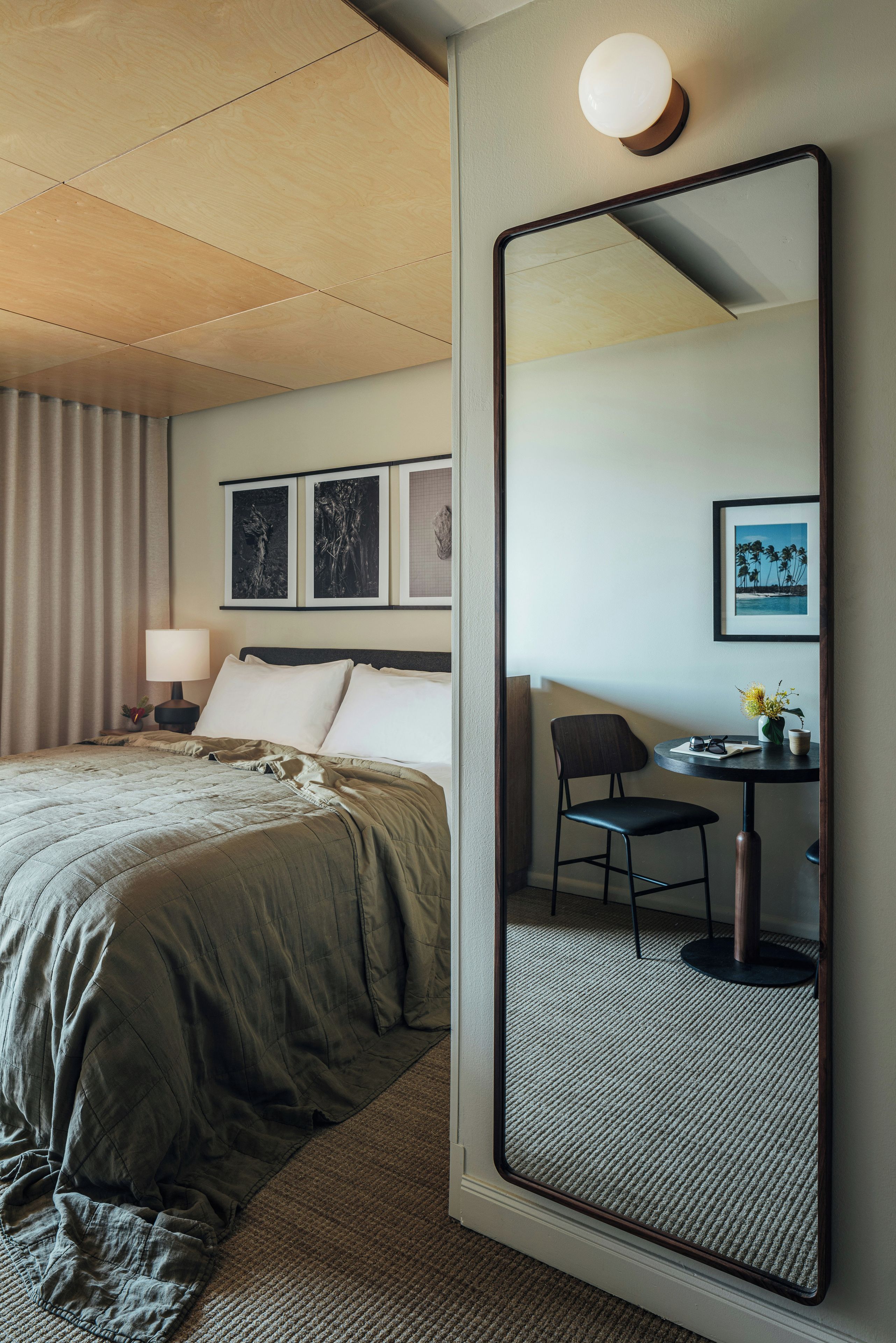 Una habitación de hotel con un espejo grande, una cama con cubierta acolchada, un escritorio con silla y cuadros enmarcados en la pared.