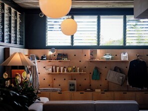Interior moderno com parede de madeira, prateleiras com produtos de higiene, luminária pendente e janela com persianas.