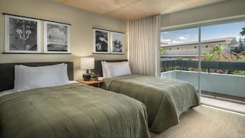A hotel room with two beds, a nightstand, a lamp, and a large window with a view of a building and greenery.