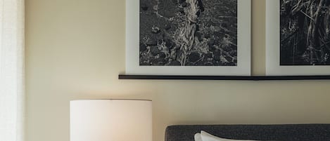 A bedroom with a bed, a bedside table with a lamp, and two framed pictures on the wall.