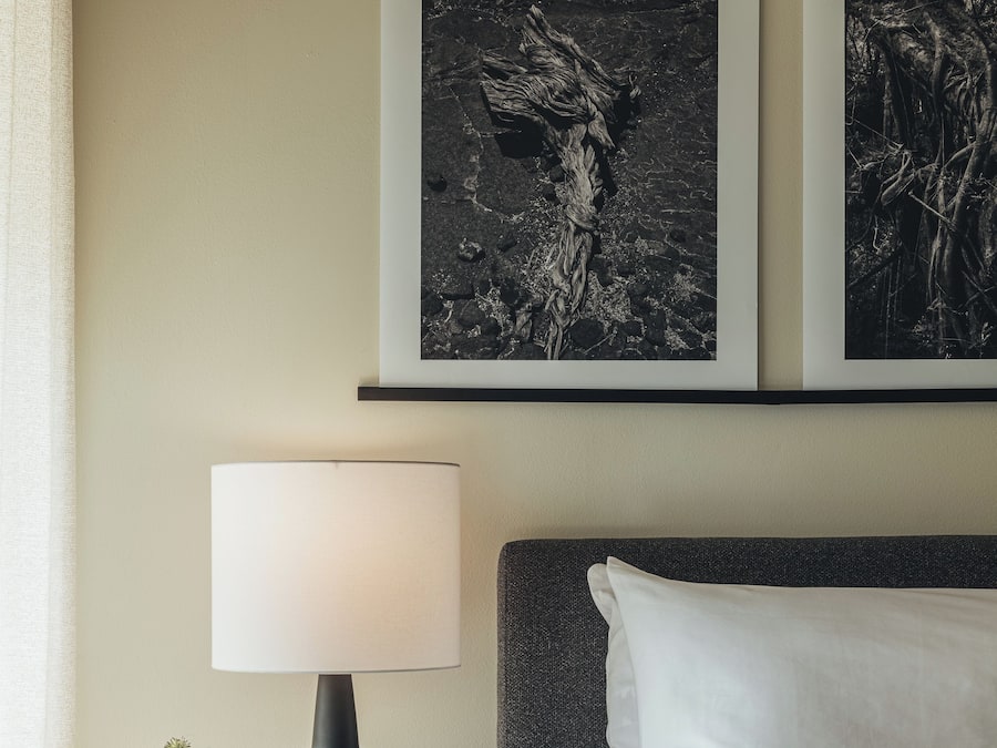 Un dormitorio con cama, una mesita de noche con lámpara y dos cuadros en la pared.