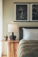 A bedroom with a bed, a bedside table with a lamp, and two framed pictures on the wall.