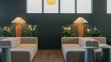 A modern waiting area with two sofas, two lamps, and potted plants.