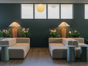 A modern waiting area with two sofas, two lamps, and potted plants.